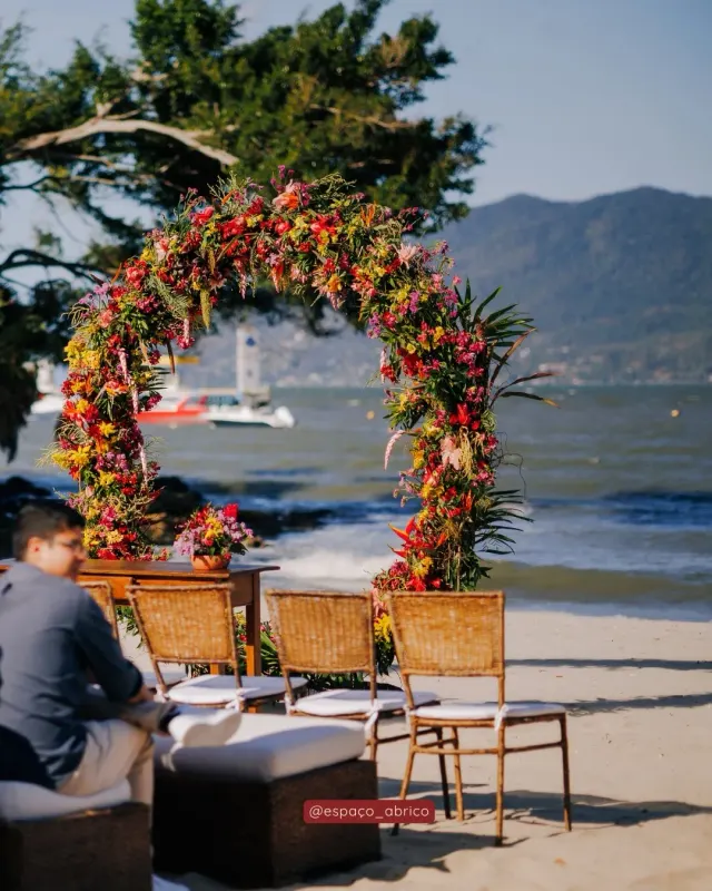 Arco de cerimônia decorado com flores coloridas na areia, em frente à baía de São Sebastião