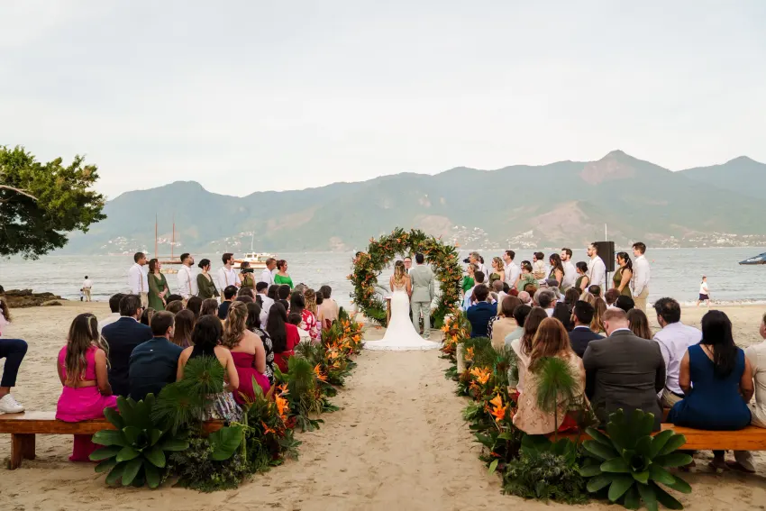 Noivos se beijando no altar à beira-mar, cercados pelos convidados