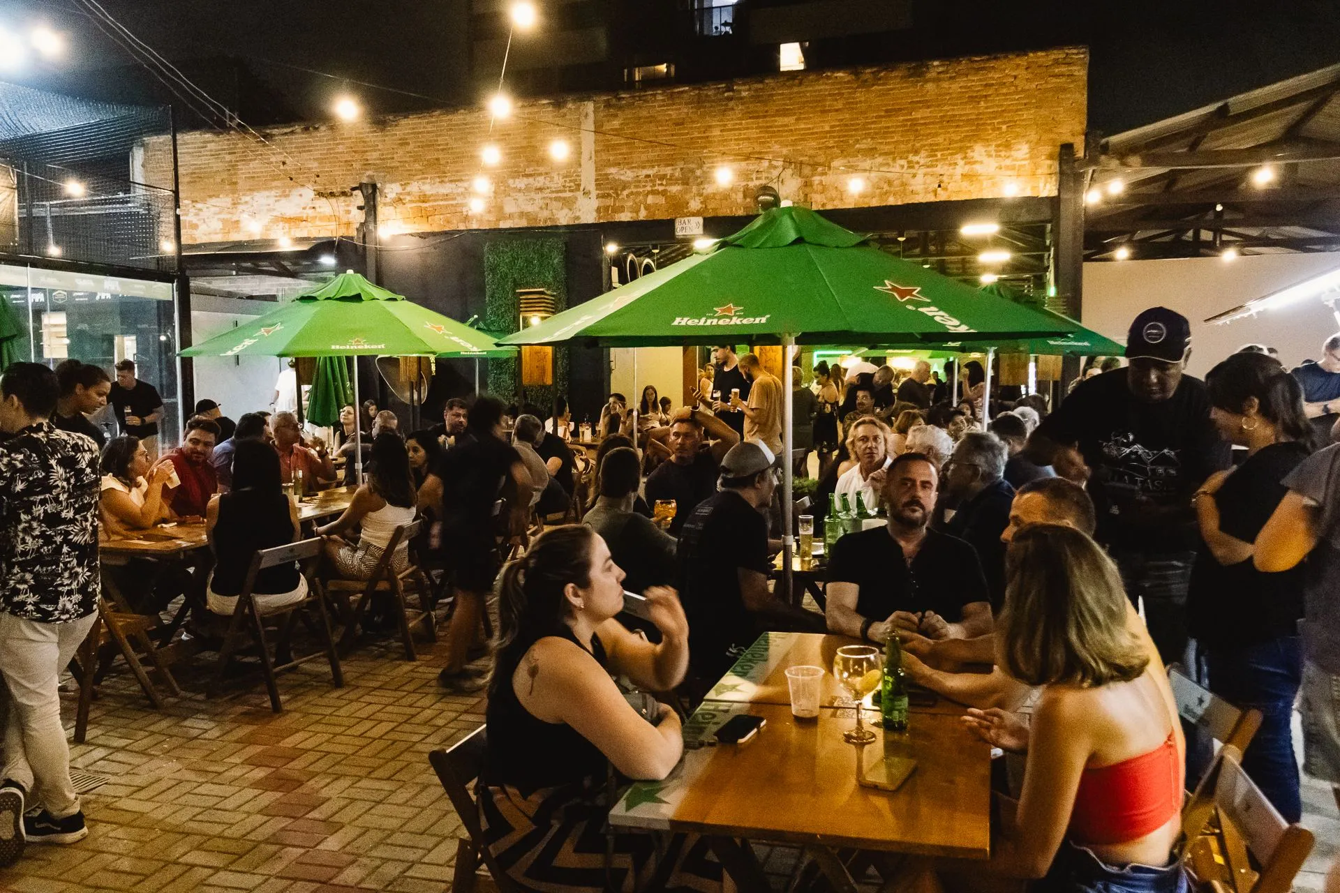 Área externa do Farofa à noite, cheia de convidados sob o varal de luzes e os guarda-sóis