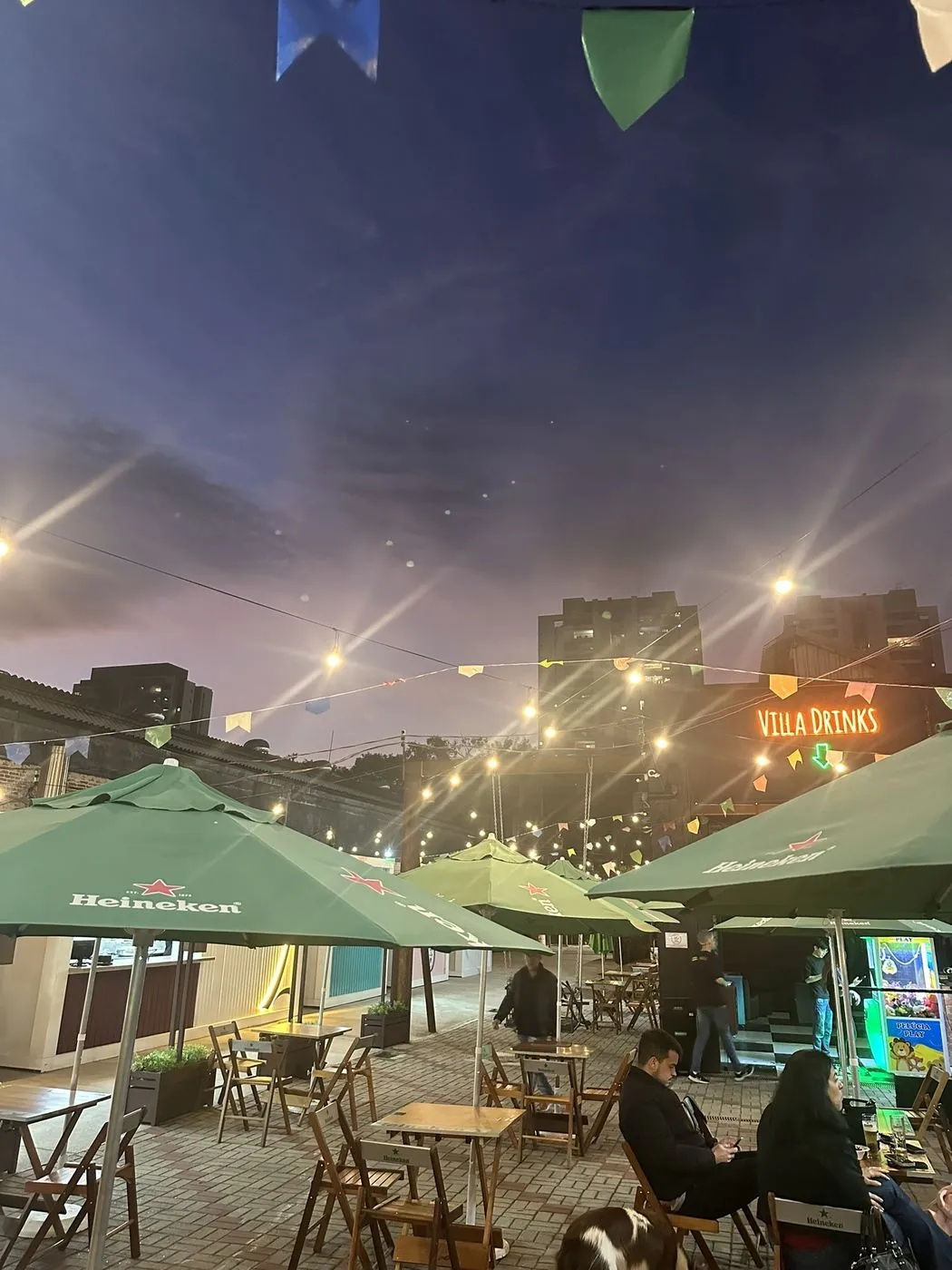 Área externa ao anoitecer com varal de luzes e guarda-sóis