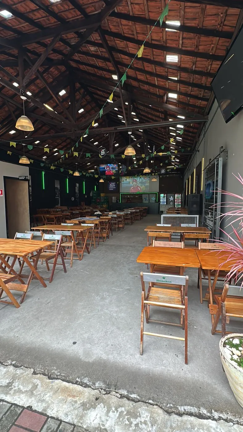 Salão interno com mesas de madeira sob o telhado do galpão