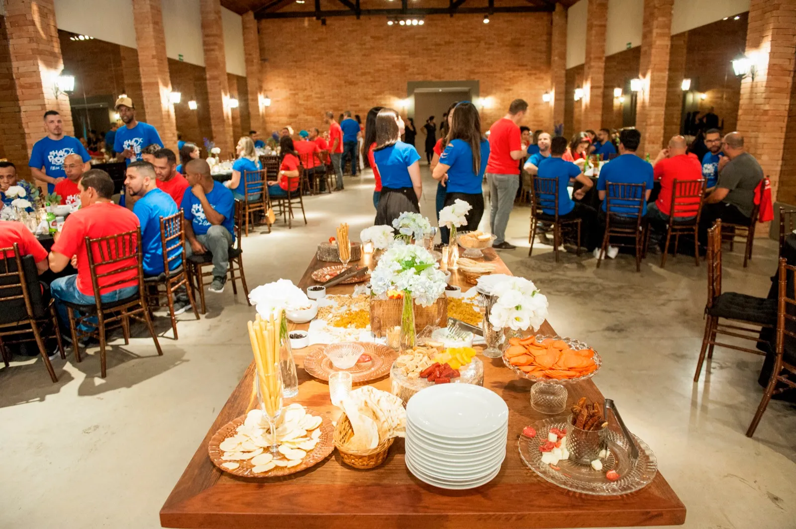 Mesa de frios e petiscos no salão com equipes ao fundo