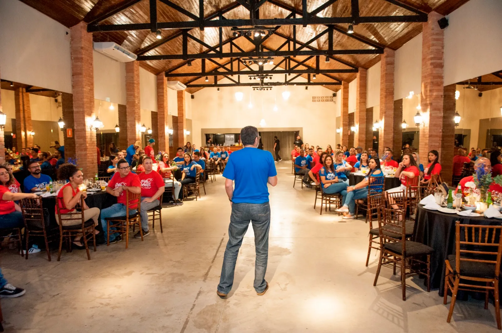 Salão da Villa Pacaembu com mesas montadas e palestrante falando para as equipes