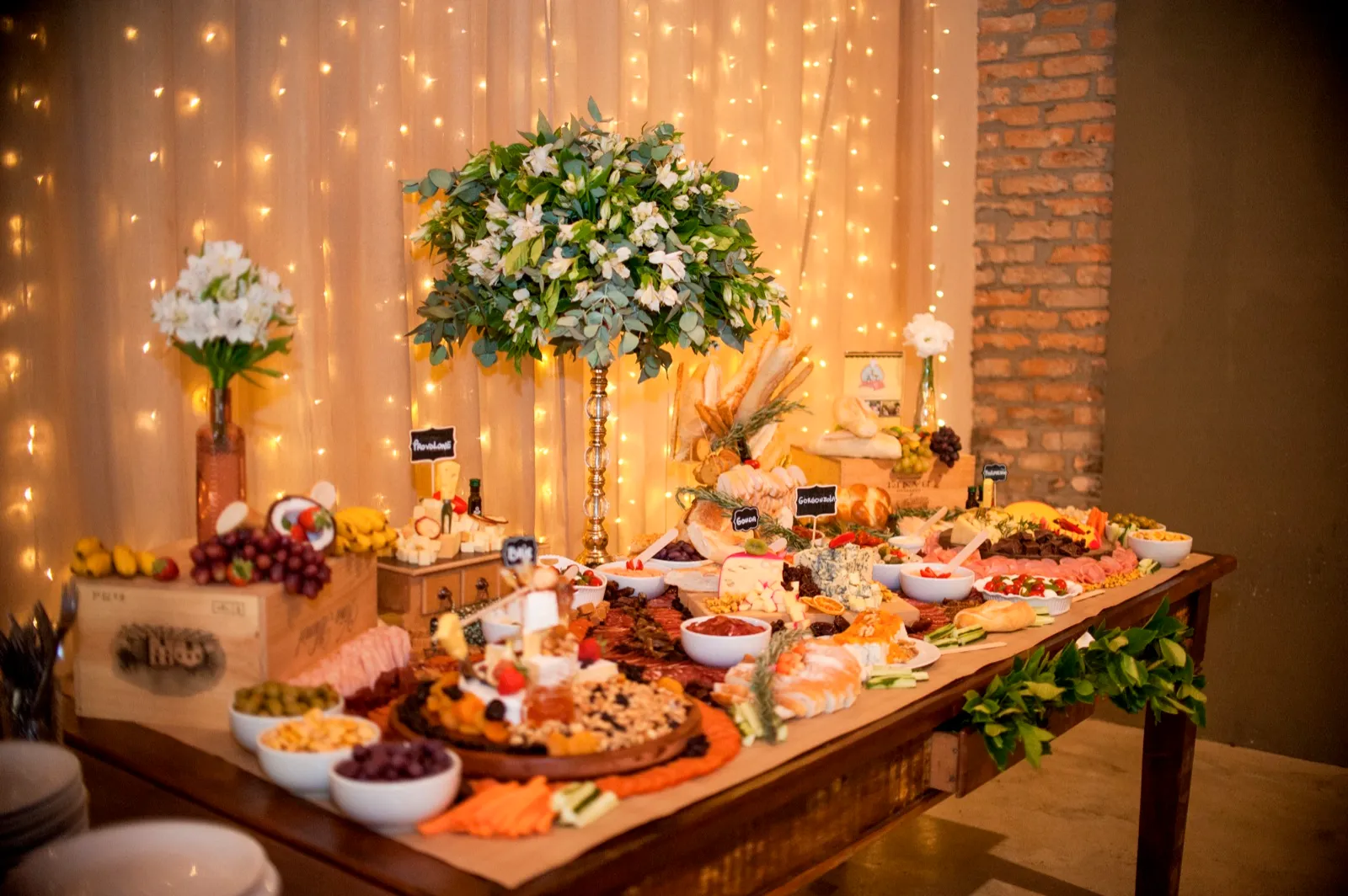 Mesa posta com frios, pães, flores e cortina de luzes